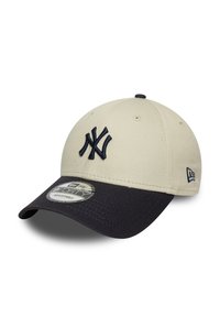 Gorra de béisbol beige con visera navy, que presenta un logotipo bordado azul en la parte delantera y un diseño redondeado en la parte trasera. Incluye una etiqueta de tamaño en la visera.