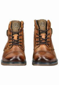 Botas de tobillo de cuero marrón con punteras redondas, superficie texturada, cordones marrones en contraste y un forro interior gris claro. Dos apliques metálicos.