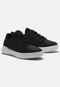 Black sneakers with a textured upper, round toe, and white rubber sole. Features include laces and a small logo on the side.