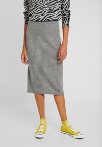Jupe midi grise à côtes fabriquée en un tissu tricot doux, présentant une silhouette ajustée et associée à des baskets jaunes montantes.