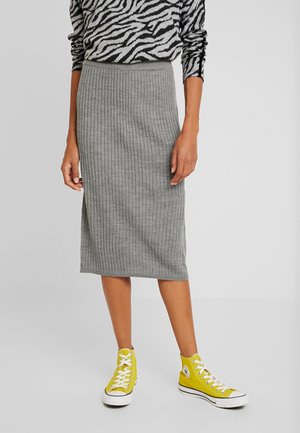 Jupe midi grise à côtes fabriquée en un tissu tricot doux, présentant une silhouette ajustée et associée à des baskets jaunes montantes.
