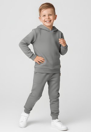 Szara bluza z kapturem i spodnie dresowe z miękkiego materiału, z kieszenią kangurką i ściągaczami, zestawione z białymi trampkami.
