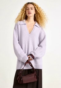 Pull surdimensionné de couleur violet clair avec un col en V et un col, fabriqué en matériau doux. Associé à un petit sac à main bordeaux avec une bandoulière.