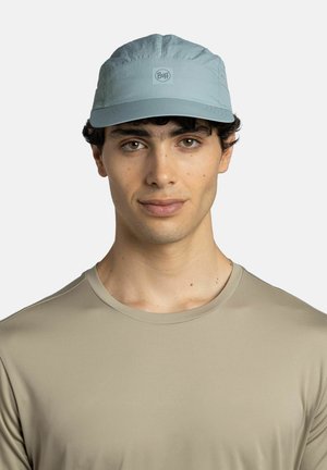 Young man with brown eyes wearing a light blue Buff cap and a beige crewneck shirt, facing forward against a plain background.