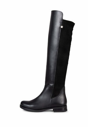 Bota negra hasta la rodilla con parte delantera de cuero liso y parte trasera de ante, suela plana y pequeño tacón, mostrada de perfil sobre fondo blanco.