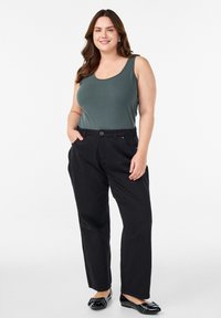 Tamnozeleni majica na bretele, crne široke hlače s džepovima i crne baletanke sa dekorativnim hardverom. Glatke teksture tkanine.