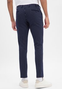 Granatowe spodnie w prążki wykonane z teksturowanej tkaniny, z dwoma tylnymi kieszeniami i wąskim krojem. Połączone z białymi trampkami.