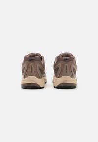 Bruna sportskor med ovandel i mesh, beige detaljer, vadderad krage och strukturerad sula; har synligt varumärke på baksidan.