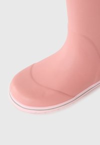 Botte de pluie en caoutchouc rose avec un bout arrondi, présentant une texture lisse et une semelle rayée blanche et grise.
