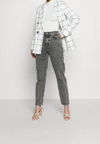 Jeans grises de cintura alta con una silueta relajada, combinados con un blazer blanco de estampado de cuadros y sandalias de tacón alto blancas con la puntera descubierta.