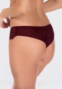 Burgundowe majtki z połączeniem przezroczystego i koronkowego materiału. Posiadają gładką tylną część oraz delikatne koronkowe wykończenie z jednej strony, charakteryzując się gładką, miękką fakturą.