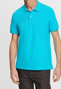 Polo turquoise en coton doux avec un col classique, une patte de boutonnage à deux boutons et des manches courtes. Texture lisse sans motifs visibles.