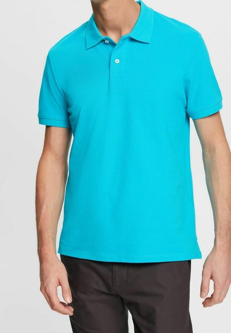 Polo turquoise en coton doux avec un col classique, une patte de boutonnage à deux boutons et des manches courtes. Texture lisse sans motifs visibles.