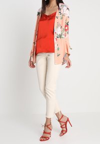 Persikofärgad blommig kimono över en röd satinkamisol, kombinerad med krämfärgad tapered jeans och röda remsandaler med hög klack.