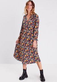 Blumen Midi-Kleid mit schwarzem Hintergrund, das lebhafte orange, gelbe und pinke Blumen zeigt. Lange Ärmel mit elastischen Bündchen. Schwarze Knöchelschäfte.