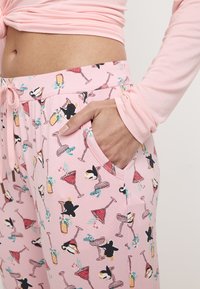 Pantalones de pijama rosa claro con un patrón repetido de pingüinos, cócteles y decoraciones tropicales; cuentan con una cinturilla elástica y bolsillos.