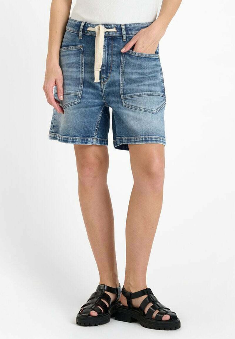 Shorts en denim bleu clair avec une coupe décontractée, comportant deux poches avant, une taille élastique avec cordon de serrage, et un ourlet effiloché. Portés avec des sandales noires.