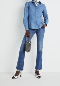 Ljusblå denimskjorta med knappstängning, ihop med ljusblå flarejeans. Silverfärgade klackskor och en svart nystartad handväska.