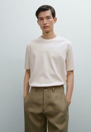 Lys beige t-shirt med korte ærmer og rund udskæring, kombineret med højtaljede olivengrønne bukser med sidelommer og knaplukning.