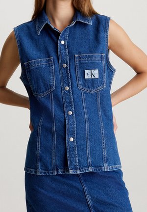 Gilet sans manches en denim bleu avec boutons, comportant deux poches poitrine, dont une avec un petit patch logo Calvin Klein.