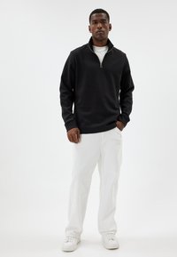 Black zip-up sweatshirt with long sleeves, paired with white pants and white sneakers. Smooth fabric with a stand-up collar design.