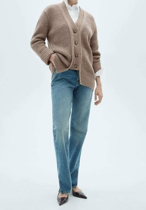 Brauner gestrickter Cardigan mit V-Ausschnitt und fünf Knöpfen, kombiniert mit blauen geraden Jeans und dunklen spitzen Schuhen.
