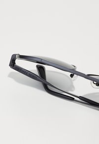 Occhiali da sole Michael Kors neri con montatura in plastica elegante, con cuscinetti nasali trasparenti e dettagli del logo sulle aste. Design minimalista con finitura liscia.