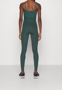 Dunkelgrünes Sportoutfit bestehend aus einem gerippten Cropped-Top und hoch taillierten Leggings, ergänzt durch schwarze Sportschuhe.