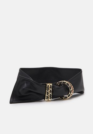 Ceinture large en similicuir noir avec une grande boucle en forme de maillon de chaîne dorée et un détail décoratif enroulé sur fond blanc.
