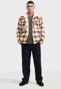 Ruuduline särkjakk beeži ja musta värviga, karvaga kraega, kombineeritud tekstuurse rohelise kampsuniga ja tumedate pükstega. Komplekti kuuluvad mustad kingad.