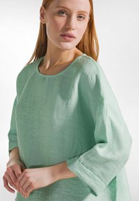 Loszittend, lichtgroen shirt met een gestructureerde, gekreukte stof. Heeft een ronde hals en driekwartmouwen. Eenvoudig ontwerp.