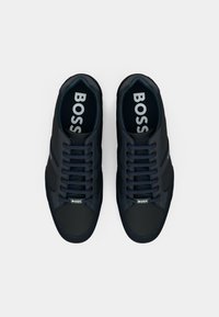 Dark blue casual sneakers with lace-up design, smooth synthetic upper, rubber sole, and prominent "BOSS" logo on the insoles.