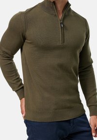 Pullover in maglina verde oliva con colletto a zip corto, polsini e orlo a coste, caratterizzato da un motivo testurizzato sulle maniche.