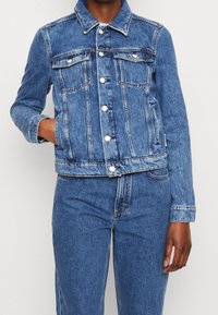 Denim jacket in light blue, featuring a classic collar, button front, and two chest pockets. Slightly faded with a cropped fit and long sleeves.