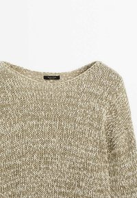 Pull en maille beige avec un col rond, posé à plat sur un fond blanc, montrant la texture et le tissage du tissu.