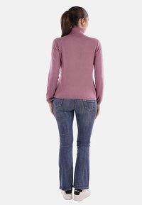 Pullover a maniche lunghe e collo alto di color lilla, dal design aderente. Abbinato a jeans scuri a campana e sneakers bianche, visto da dietro.