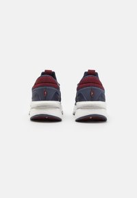 Sport-sneakers med navy overdel og burgunder detaljer, hvit mellomsåle, strukturert stoff, og en pull-tab ved hælen for enkel påkledning.