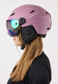 Pinkfarbener Skihelm mit matter Oberfläche, verstellbarem schwarzem Riemen, integrierter Skibrille mit irisierendem Glas und Belüftungsöffnungen.