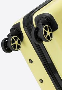 Valigia rigida di colore giallo tenue con superficie testurizzata. Presenta accessori neri e quattro ruote multidirezionali per una facile mobilità.