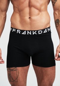 Zwarte boxershorts gemaakt van zacht materiaal met een brede elastische tailleband met contrasterende witte logotekst. Glad, aansluitend ontwerp.