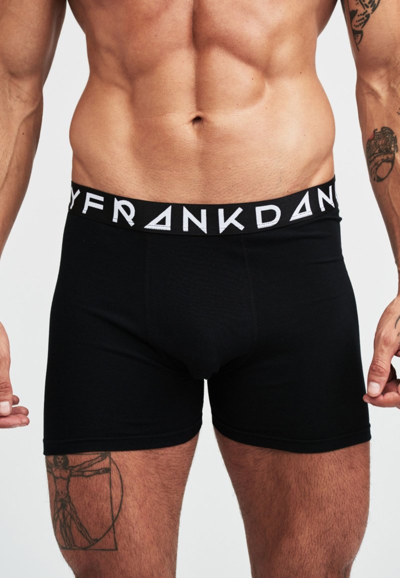 Zwarte boxershorts gemaakt van zacht materiaal met een brede elastische tailleband met contrasterende witte logotekst. Glad, aansluitend ontwerp.