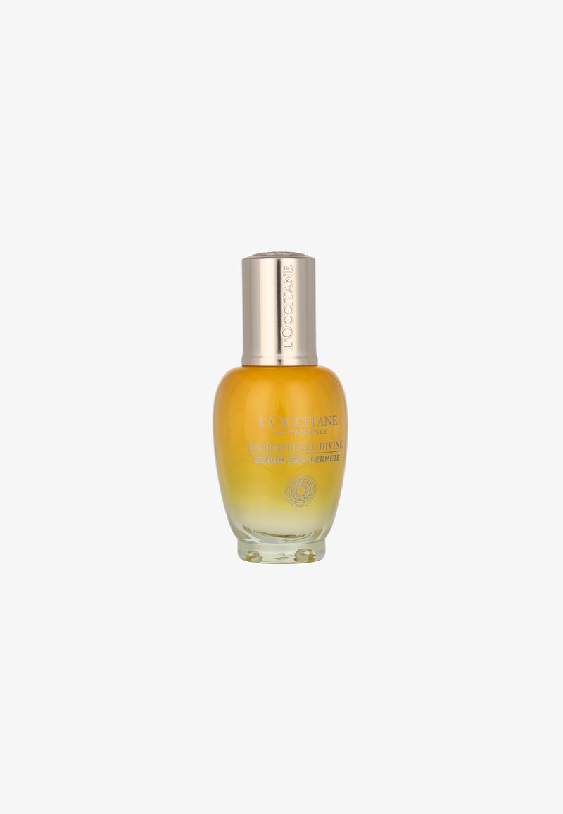 Bouteille en verre avec une base arrondie, un col conique et un capuchon métallique argenté. Liquide jaune à l'intérieur, étiqueté "Sérum Pro-Fermeté."