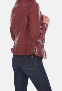 Röd läderjacka med en åtsittande design, synliga sömmar, fickor med dragkedja och justerbara detaljer i midjan, i kombination med blåjeans.