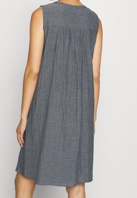 Robe sans manches, longueur genou, de couleur gris foncé, avec une texture froissée et un design froncé dans le dos, mettant en avant une coupe décontractée.