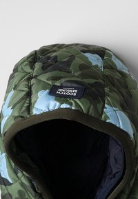 Capucha acolchada en camuflaje verde con acentos en azul claro. Presenta un ribete oscuro y un parche con el logo que se muestra de manera prominente en la parte frontal.
