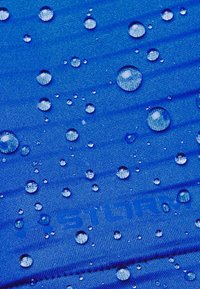 Des gouttes d'eau perlaient sur un tissu texturé bleu étiqueté "STORM", indiquant un matériau résistant à l'eau.