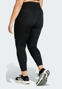 Black athletic leggings with a high waist, smooth fabric, and reflective accents. Pairing with black sneakers featuring white stripes and a cushioned sole.