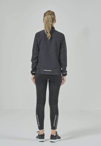 Svart sportjacka med hög krage, tillsammans med svarta leggings som har strukturerade paneler och vit "ENDURANCE" text längs sidorna.
