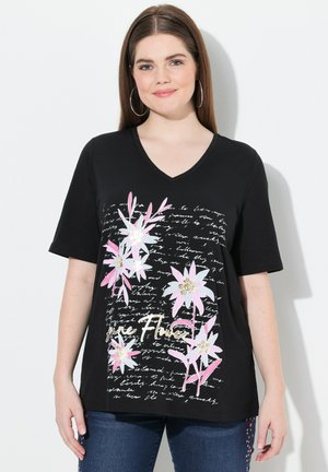 Zwarte V-hals T-shirt met een bloemmotief in roze en wit, met metallic accenten en een achtergrond met scriptpatronen. Korte mouwen.