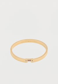 Χρυσό βραχιόλι Tommy Hilfiger με ραβδωτή υφή, μικρά κρύσταλλα στο κούμπωμα και χαραγμένο το όνομα της μάρκας στο εσωτερικό της ταινίας.